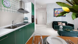 Eine moderne Küche mit grünen Schränken, einer weißen Arbeitsplatte und einer Uhr. Es gibt einen Essbereich mit einem grünen Sofa und einem Bild an der Wand.