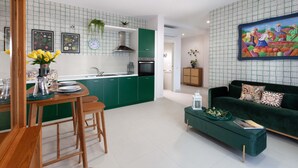Eine moderne Küche mit grünen Schränken, ein Essbereich mit Holzmöbeln und ein grünes Sofa im Wohnzimmer.