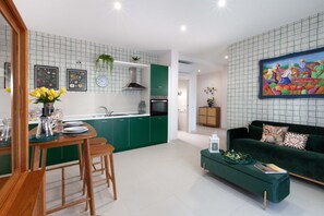 Eine moderne Küche mit grünen Schränken, ein Essbereich mit Holzmöbeln und ein grünes Sofa im Wohnzimmer.