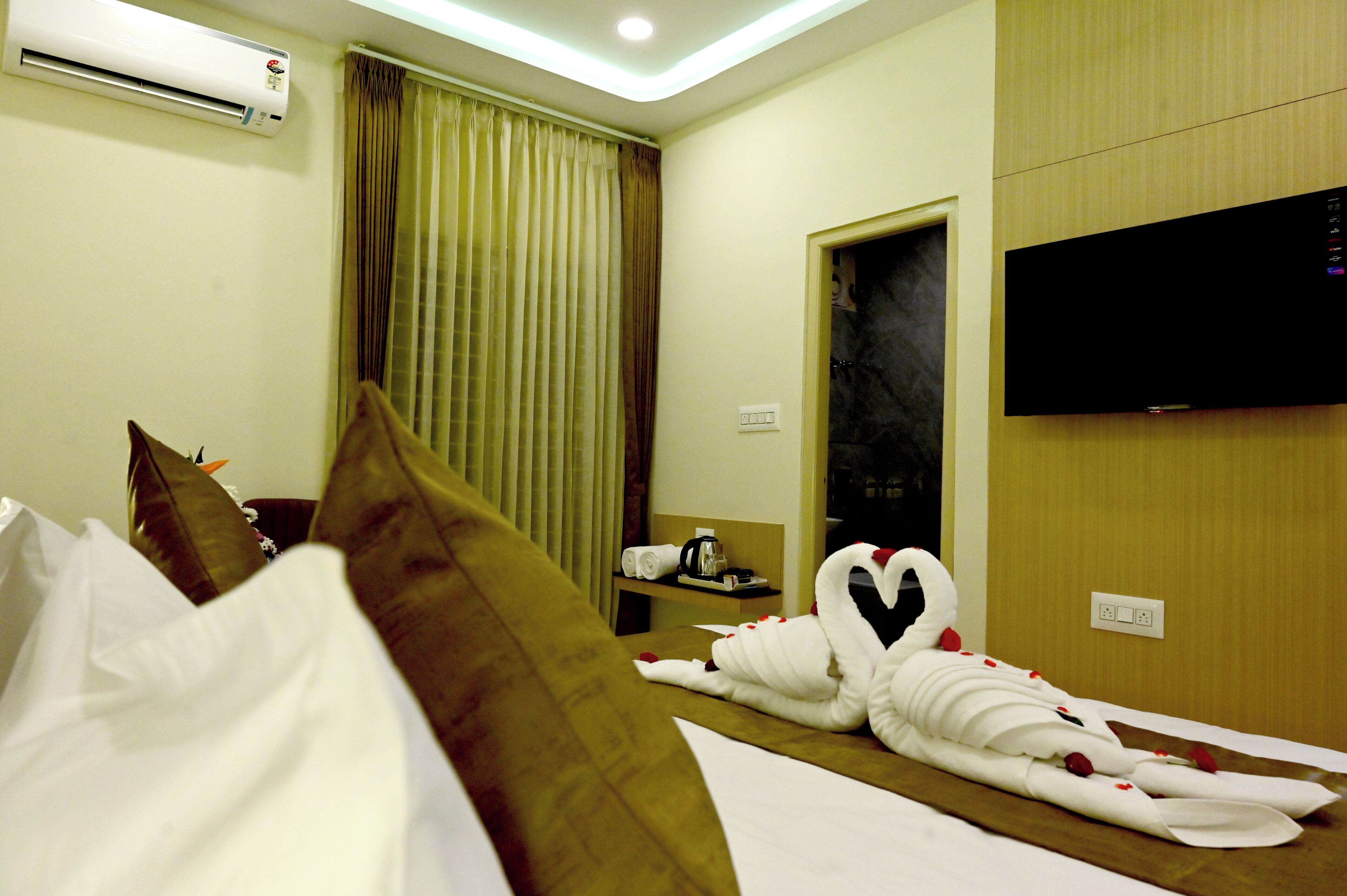 A hotel room with a bed, pillows, a TV, and a window with curtains.