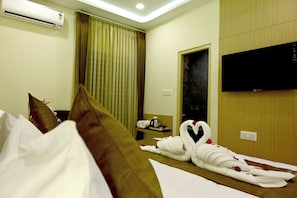 A hotel room with a bed, pillows, a TV, and a window with curtains.