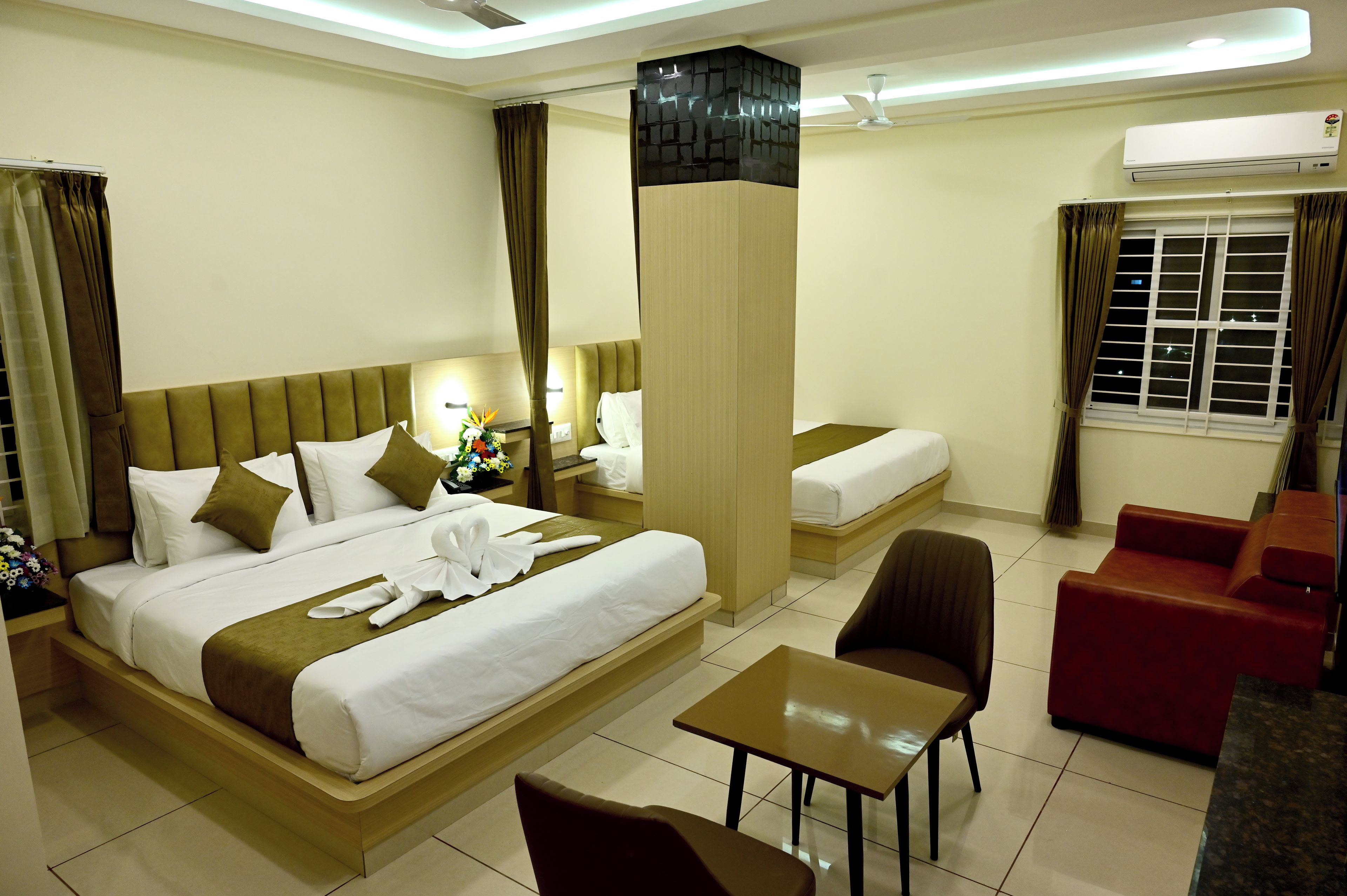 A hotel room with a large bed, a smaller bed, a desk, a chair, and a sofa.