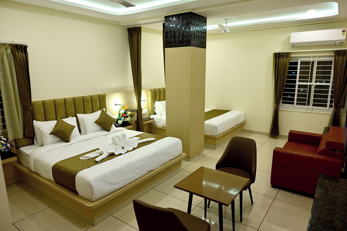 Ein Hotelzimmer mit einem großen Bett, einem kleineren Bett, einem Schreibtisch, einem Stuhl und einer Couch.