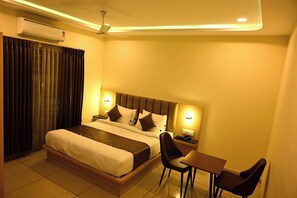 A hotel room with a bed, bedside table, chair, and a small table. - S R GRAND (Tumkur)
