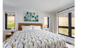 Un dormitorio con una cama grande, un cabecero de madera y dos ventanas con cortinas.