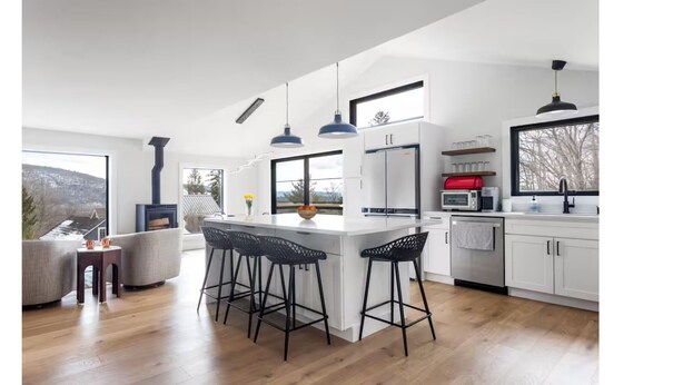Una cocina moderna con una isla central, taburetes de bar y vistas al exterior.