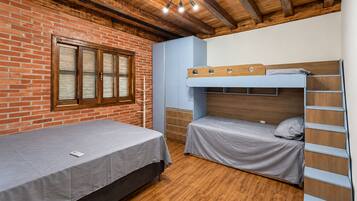Una habitación con pared de ladrillo, vigas de madera en el techo, una cama litera y una cama individual.