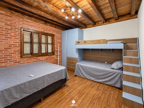 A room with a brick wall, wooden ceiling beams, a bunk bed, and a single bed.