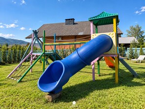 A playground with a slide, climbing structures, and a house in the background. - Sítio Recanto Pedacinho do Céu - Camboriú/SC (Camboriú)