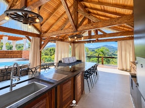 A spacious outdoor kitchen area with a large island, bar stools, and a view of lush greenery. - Sítio Recanto Pedacinho do Céu - Camboriú/SC (Camboriú)