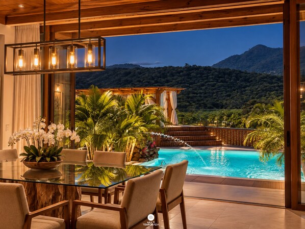A modern outdoor dining area with a glass table and chairs, overlooking a swimming pool and a mountainous landscape. - Sítio Recanto Pedacinho do Céu - Camboriú/SC (Camboriú)