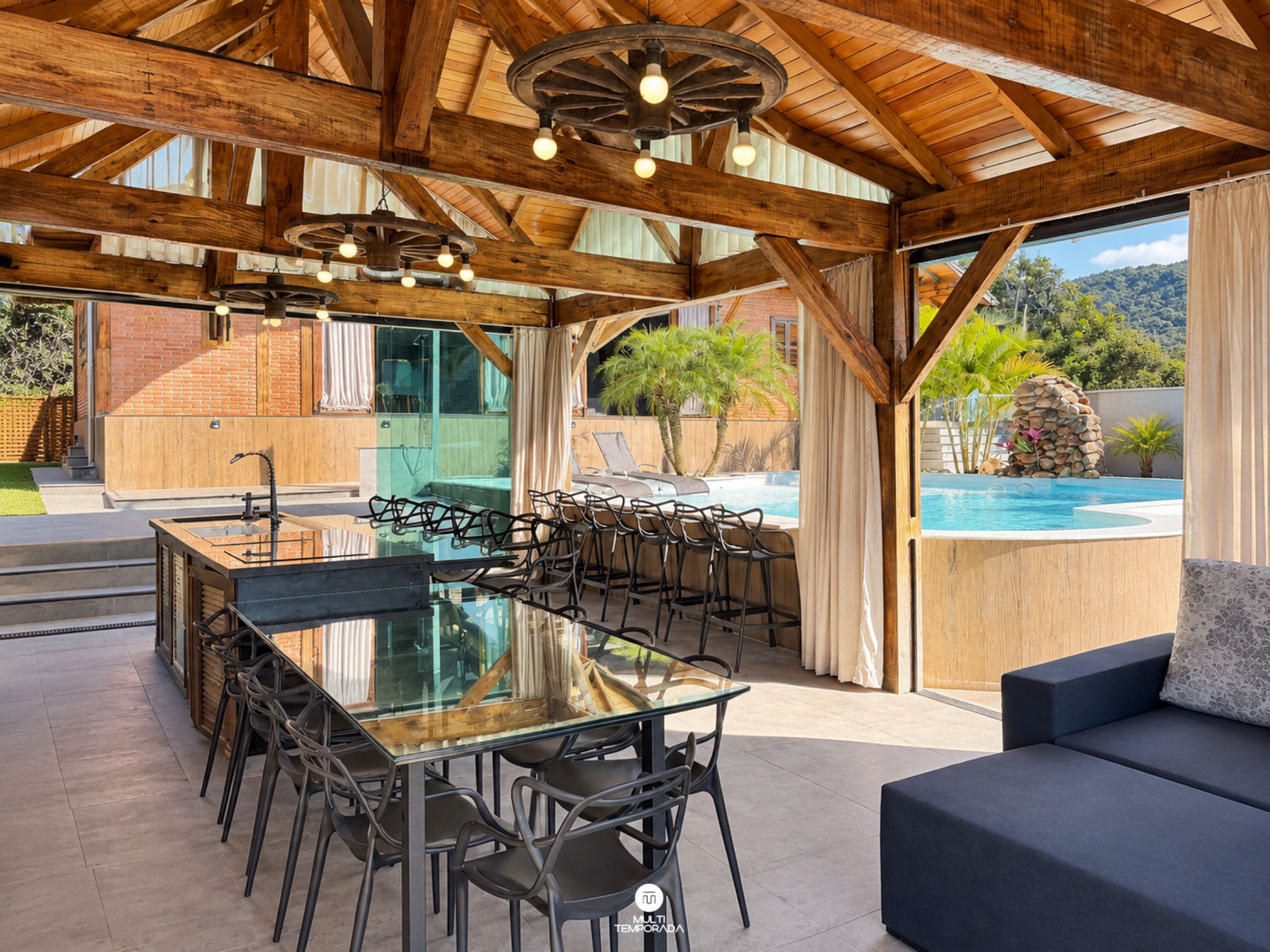 An outdoor dining area with a glass-top table and chairs, a pool, and a view of a mountainous landscape.