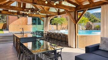 An outdoor dining area with a glass-top table and chairs, a pool, and a view of a mountainous landscape.