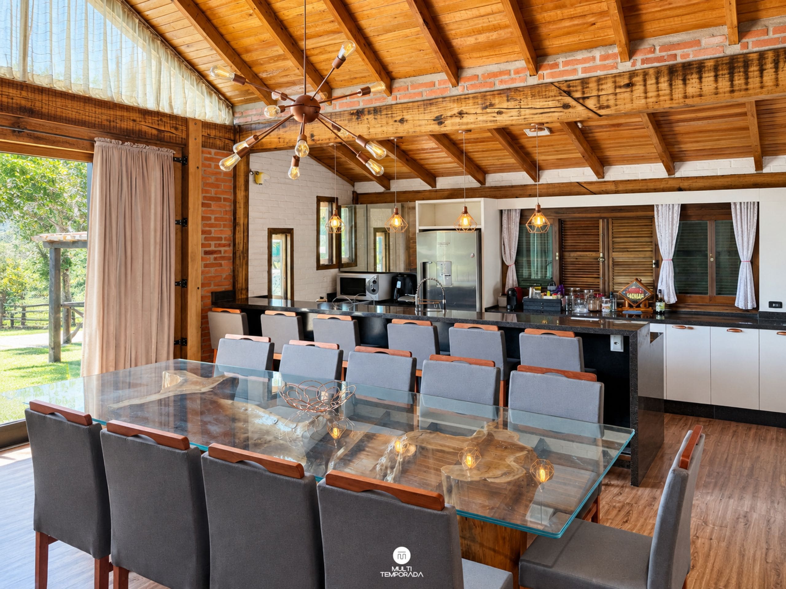 Un comedor amplio con una mesa y sillas de vidrio, una cocina con armarios blancos y un techo de madera.