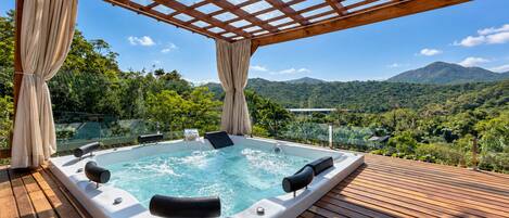 A hot tub with a wooden deck and a view of a mountainous landscape.