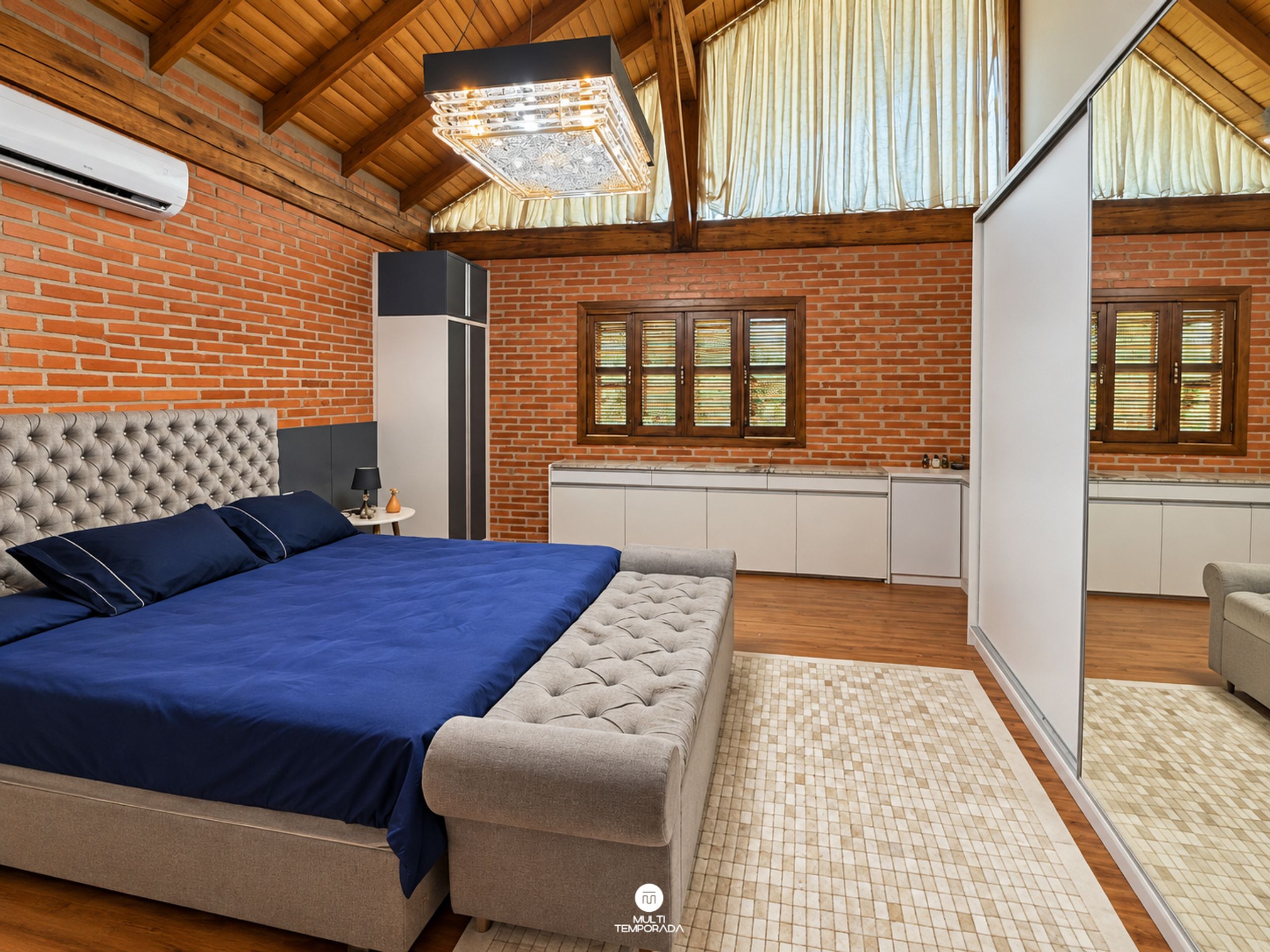 Un dormitorio con una cama grande, techo de madera, pared de ladrillo y una ventana con contraventanas.