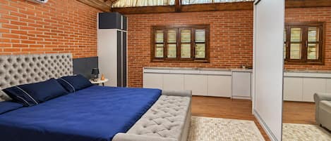 Un dormitorio con una cama grande, techo de madera, pared de ladrillo y una ventana con contraventanas.
