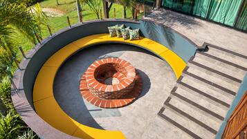 Una escalera en espiral con un núcleo de ladrillo, rodeada de escalones amarillos y grises, que conduce a un balcón con vistas a un jardín.