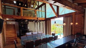 A spacious dining area with a long table and chairs, a kitchen area with a stove, and a view of the outdoors through large windows. - Sítio Recanto Pedacinho do Céu - Camboriú/SC (Camboriú)