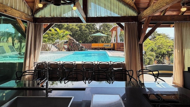 A covered outdoor seating area with a pool view, wooden beams, and a hanging light fixture. - Sítio Recanto Pedacinho do Céu - Camboriú/SC (Camboriú)