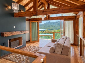 A spacious living area with a wooden ceiling, a sofa, a chessboard, and a view of a mountainous landscape.