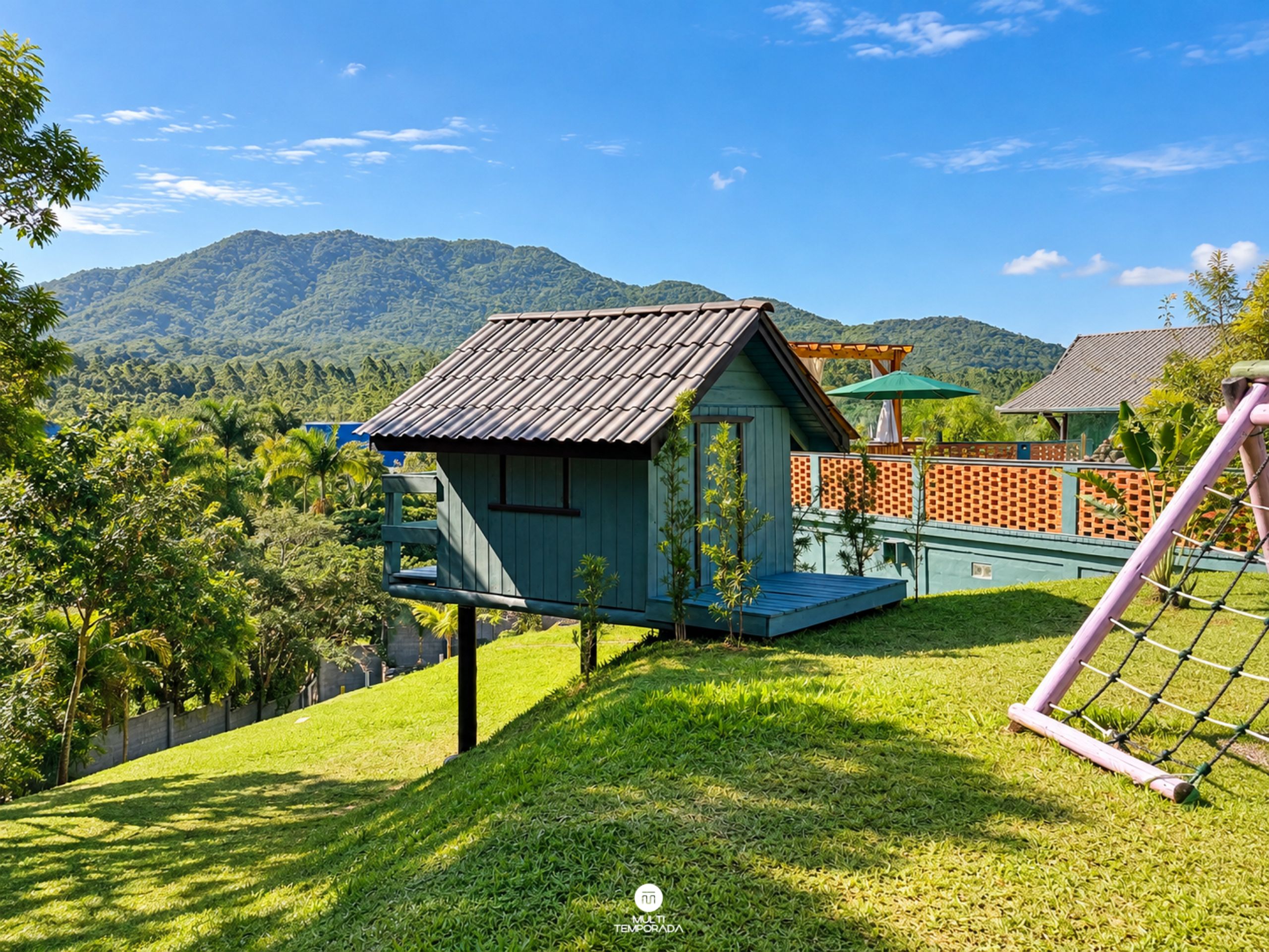 A small, elevated wooden structure with a sloped roof, surrounded by lush greenery and a mountainous backdrop.
