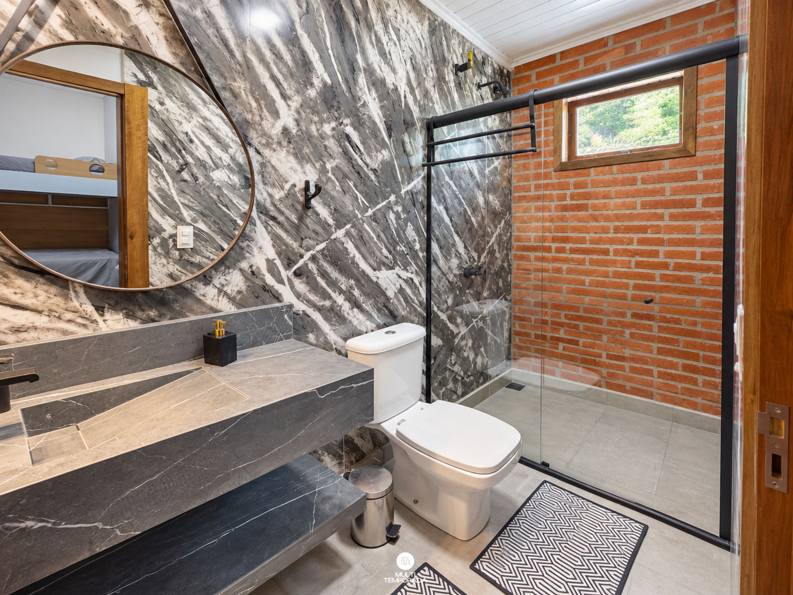Un baño moderno con pared de mármol, cabina de ducha de cristal y inodoro a la vista.