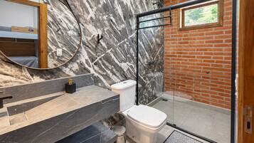 Un baño moderno con pared de mármol, cabina de ducha de cristal y inodoro a la vista.