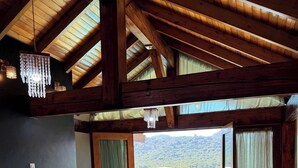 A wooden interior with a sofa, a chandelier, and a view of a green landscape. - Sítio Recanto Pedacinho do Céu - Camboriú/SC (Camboriú)