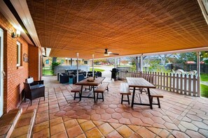 Eine Terrasse im Freien mit sechseckigen Fliesen, Holztischen und -stühlen sowie einem Grill.