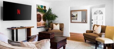 A living room with a flat-screen TV, a coffee table, sofas, and a plant.