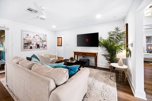 A living room with a beige sofa, a coffee table, a TV, and a potted plant. - Group Retreat | Hot Tub • Game Room • Walk to Main (Johnson City)