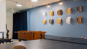 Une table de ping-pong avec une raquette de tennis de table, une table de baby-foot et un mur orné de chapeaux.