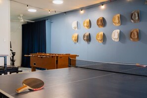 A ping pong table with a table tennis paddle, a foosball table, and a wall with mounted hats. - Group Retreat | Hot Tub • Game Room • Walk to Main (Johnson City)