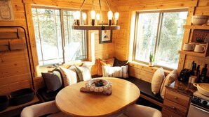 A cozy cabin interior with a wooden dining table, cushioned seating, a hanging light fixture, and a view of the forest through large windows. - Private Sauna I 1.7 mi to Lutsen Mountain I Ski I Bike I Hike (Lutsen)