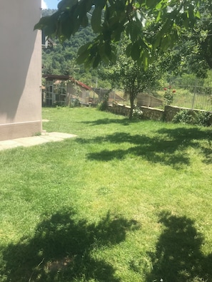Un jardín con césped, un muro de piedra, una valla metálica y un edificio al fondo.