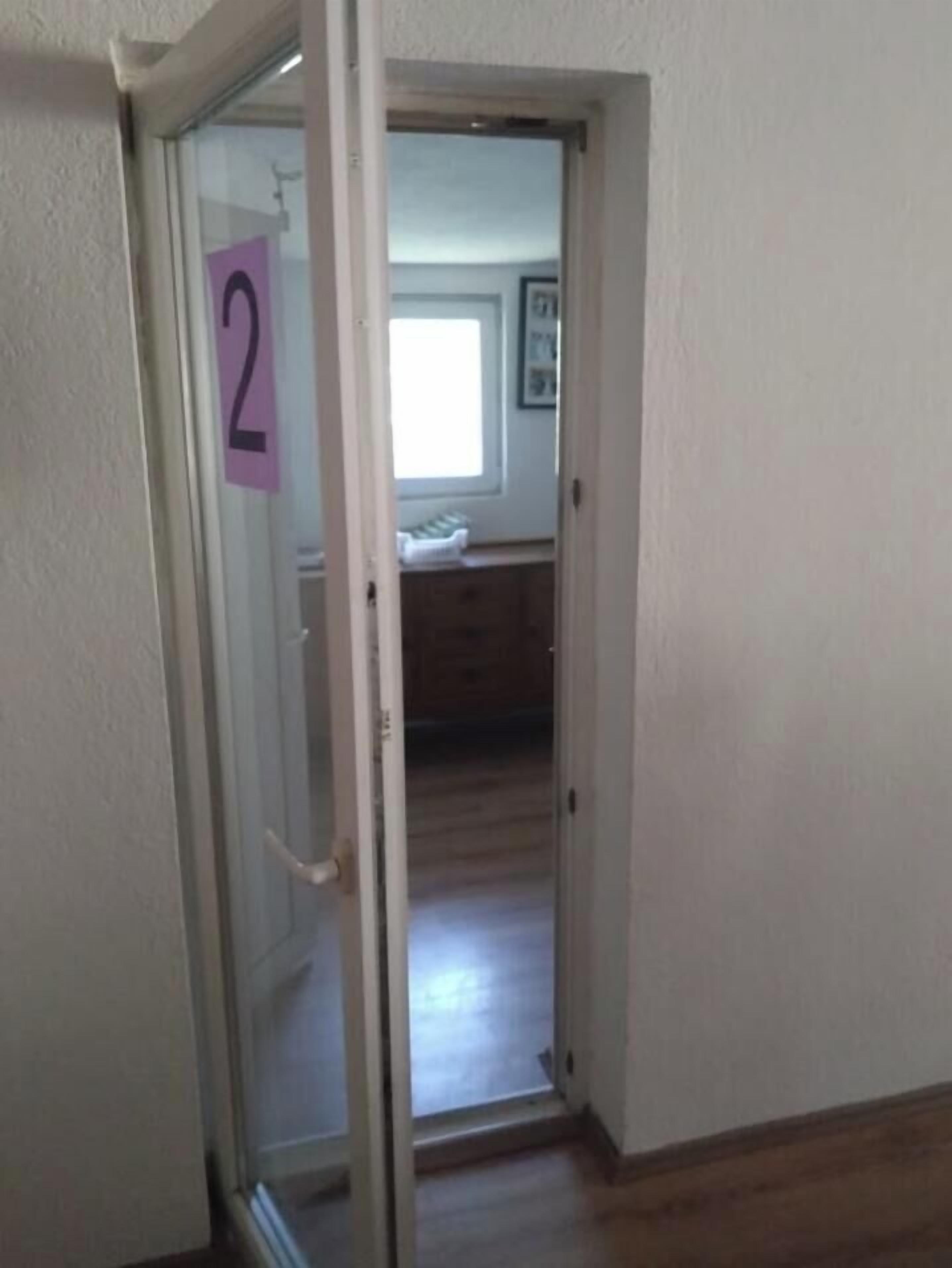 Eine geöffnete Tür, die in einen Raum mit einem Bett und einem Fenster führt.
