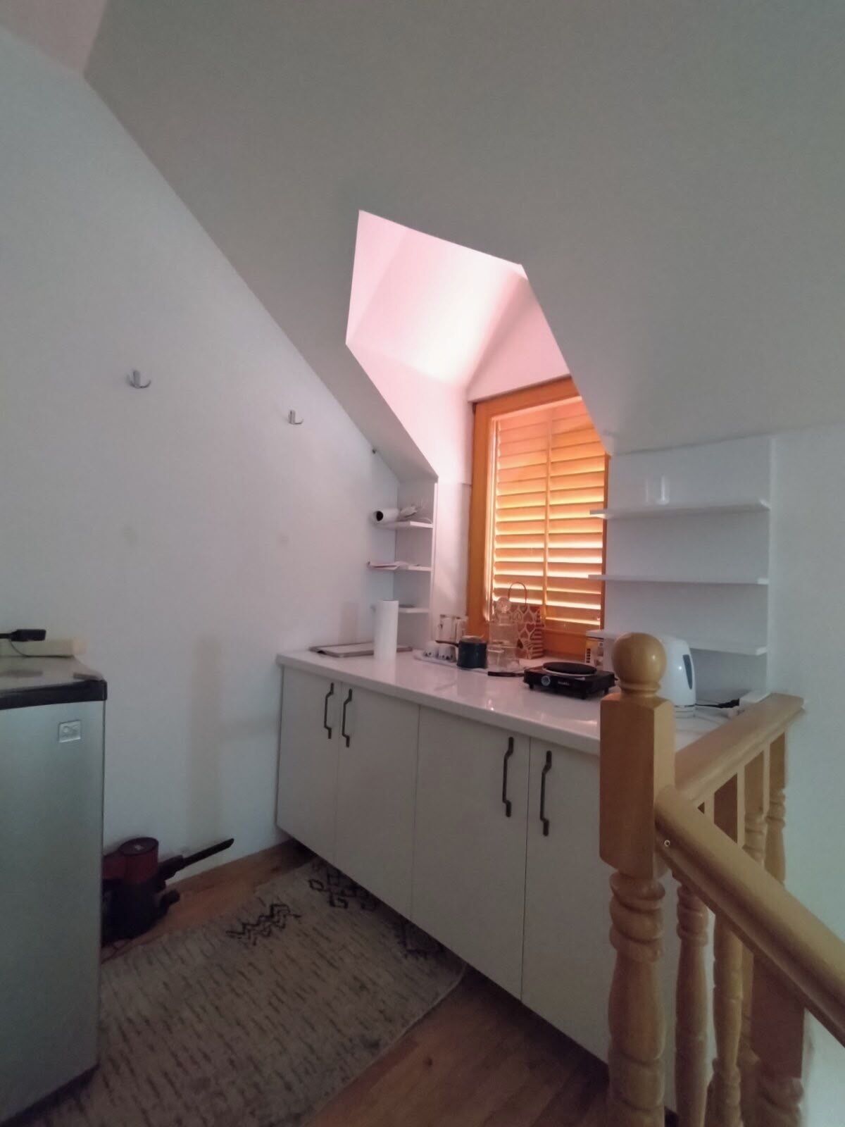 A compact kitchen with white cabinets, a small refrigerator, and a wooden staircase.