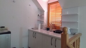 A compact kitchen with white cabinets, a small refrigerator, and a wooden staircase.
