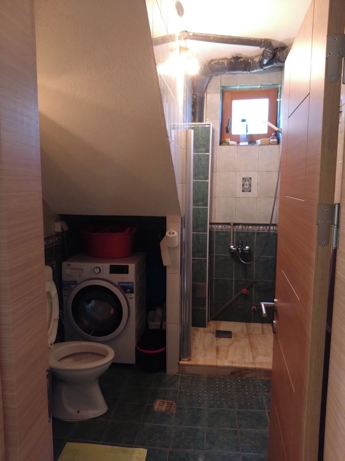 Ein kleines Badezimmer mit Waschmaschine, Toilette und Duschbereich.