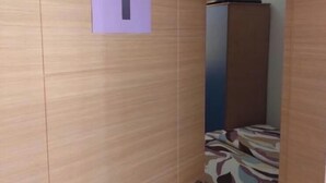 A room with a wooden door marked with the number 1, a bed with a patterned bedspread, and a small cabinet in the background.