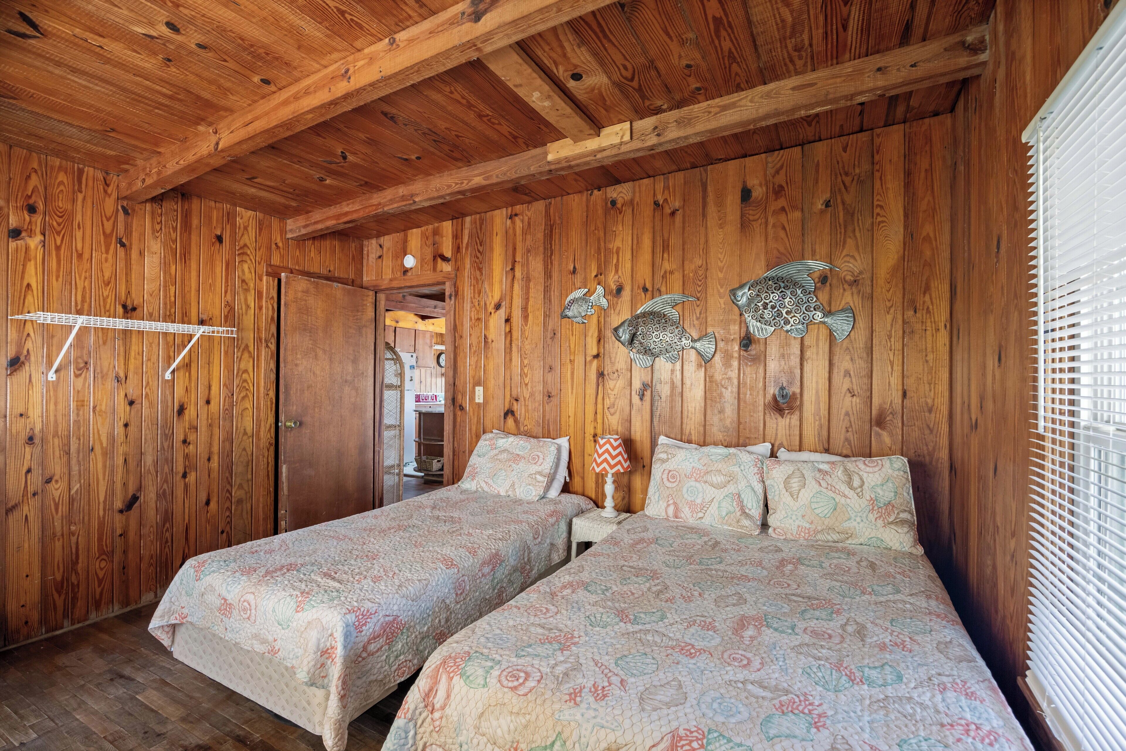 Ein Holzhütten-Zimmer mit zwei Betten, einem kleinen Tisch und einer Fischdekoration an der Wand.