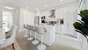 A modern kitchen with white cabinetry, a central island with bar stools, and a dining area with a marble table. - Luxury 4BR Home* Brand New & Great Location! (Ottawa)
