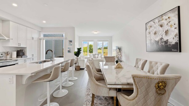 A modern kitchen with white cabinetry, a central island with bar stools, and a dining area with a marble table and upholstered chairs. - Luxury 4BR Home* Brand New & Great Location! (Ottawa)