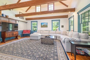 A spacious living room with a large sectional sofa, a television, and a coffee table. - Heron's Perch Beautiful Pondside Home with Screened Porch (Brunswick)