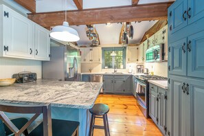 A kitchen with a central island, wooden beams, and a view of the outdoors. - Heron's Perch Beautiful Pondside Home with Screened Porch (Brunswick)