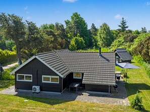 Ein zweistöckiges Haus mit dunkler Fassade, einem Ziegeldach und einer Terrasse mit Gartenmöbeln.