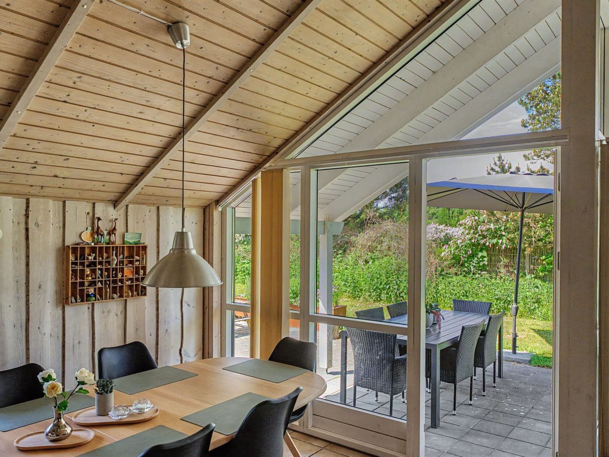 Un intérieur en bois comprenant une table à manger, des chaises, une suspension et une étagère ornée d’objets décoratifs.