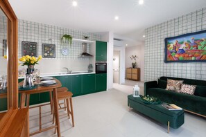 A modern kitchen with green cabinets, a dining area with wooden furniture, and a green sofa in a living room. - Estate4home - Velia in Sorrento (Sorrento)