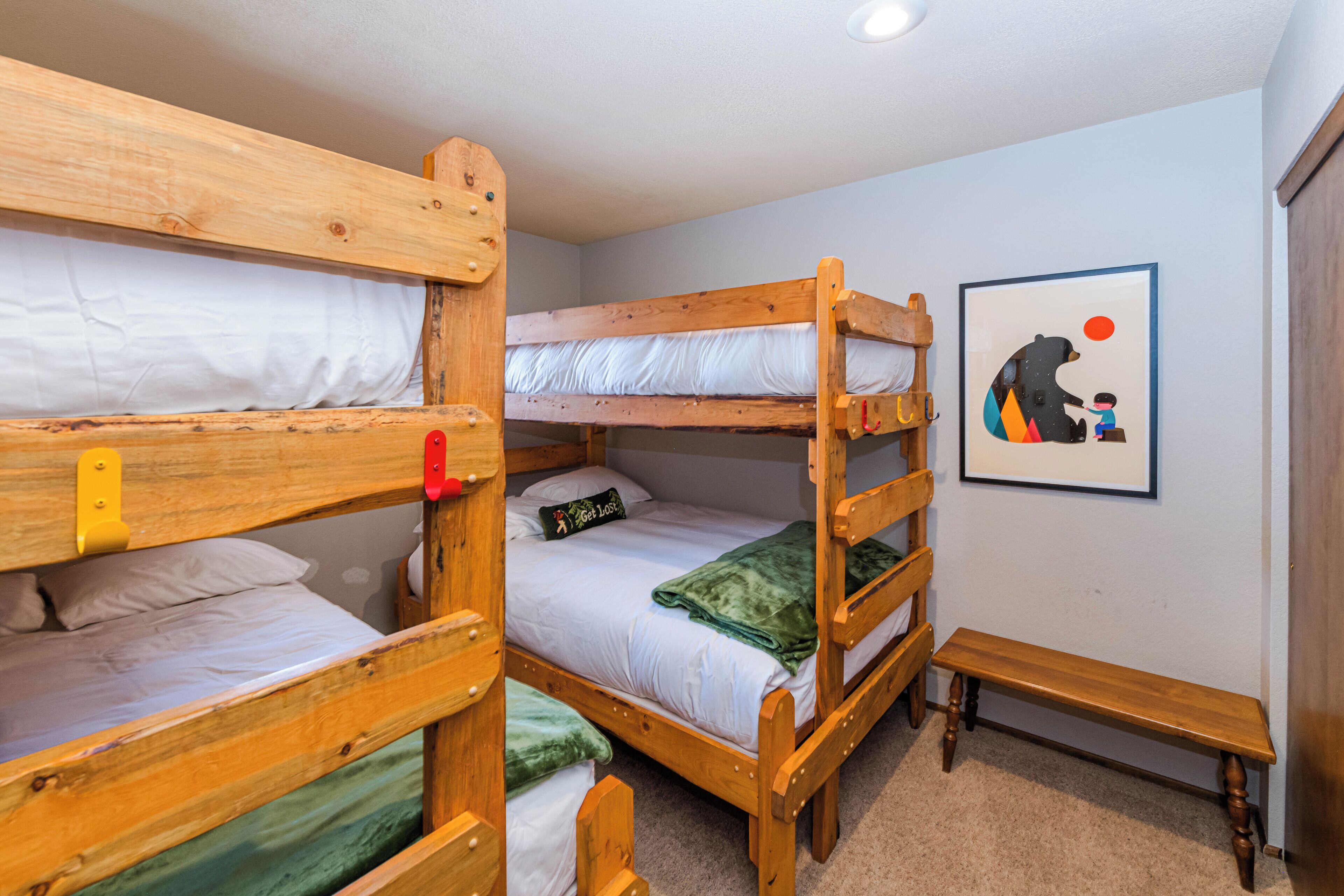 A bunk bed room with a wooden bench and a framed picture on the wall.